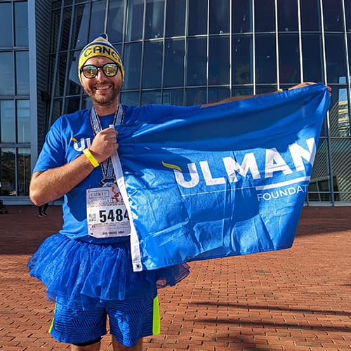 Young adult cancer survivor getting ready to run a race, holding an Ulman Foundation flag.